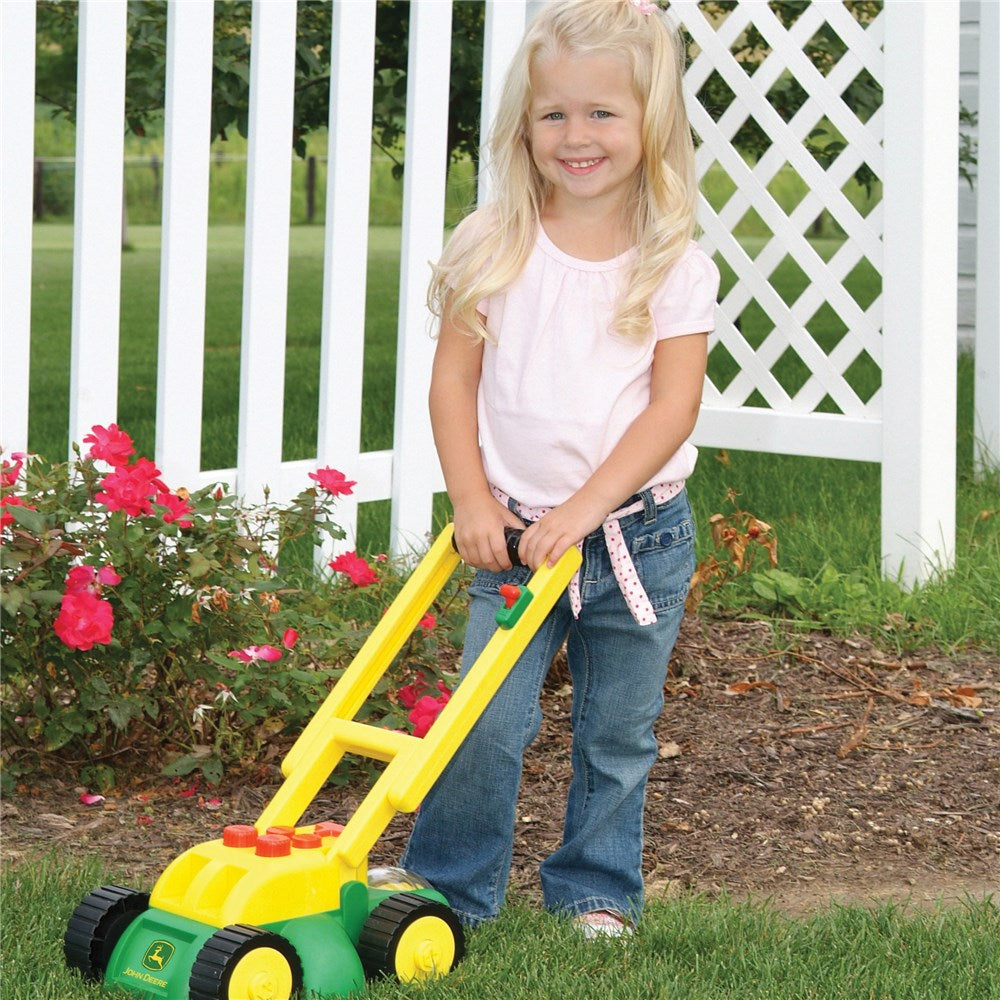 Child using John Deere Toy Real Sounds Lawn Mower in garden